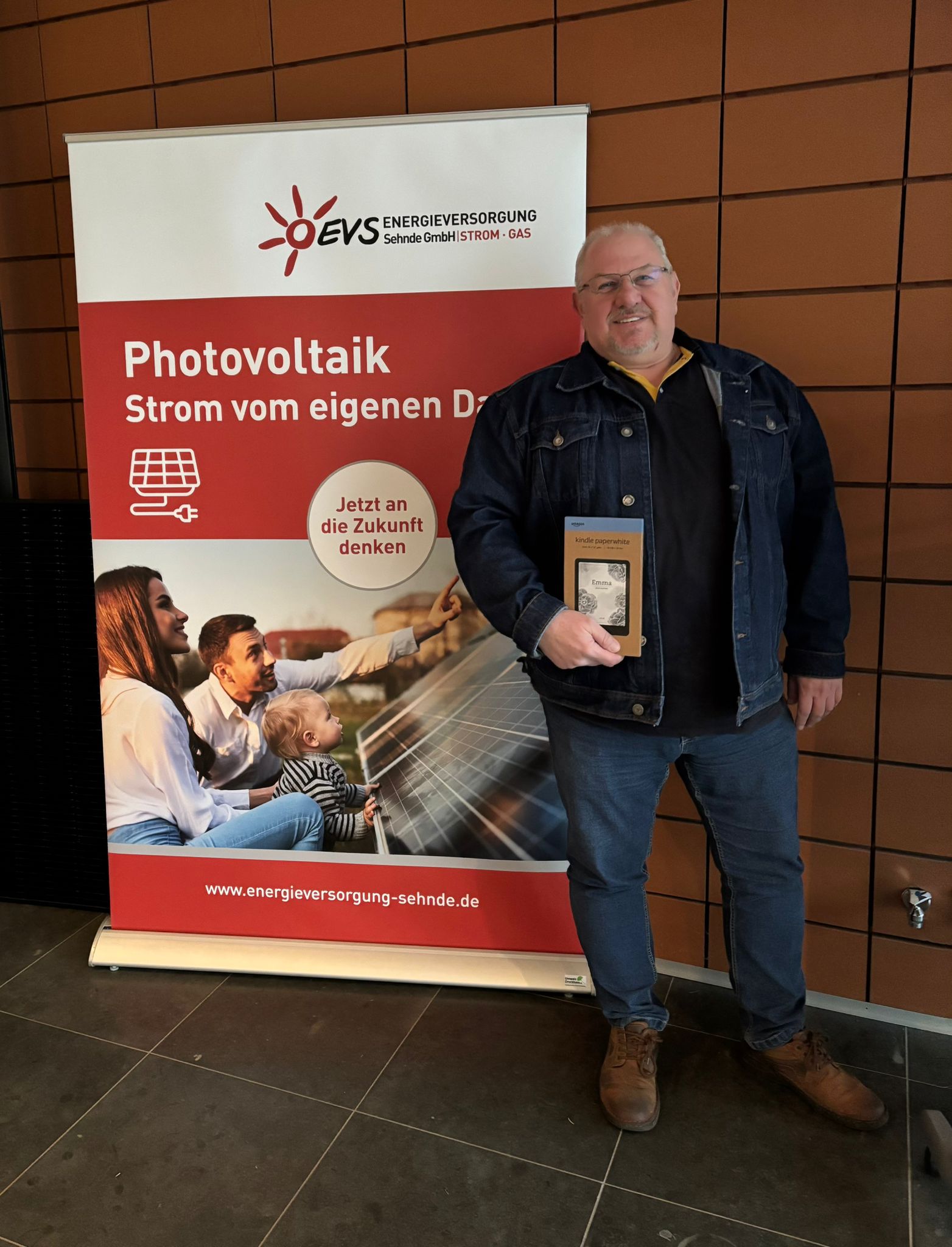 Foto von Detlef Burghardt, Gewinner des Zählerablesung-Gewinnspiels vor einem Roll-Up der EVS zum Thema Photovoltaik mit seinem E-Book-Reader in der Hand