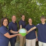 Fünf Personen in blauen Poloshirts stehen vor grünem Laub und halten gemeinsam einen grünen und weißen Ball mit dem Logo ‚Energieversorgung Sehnde‘